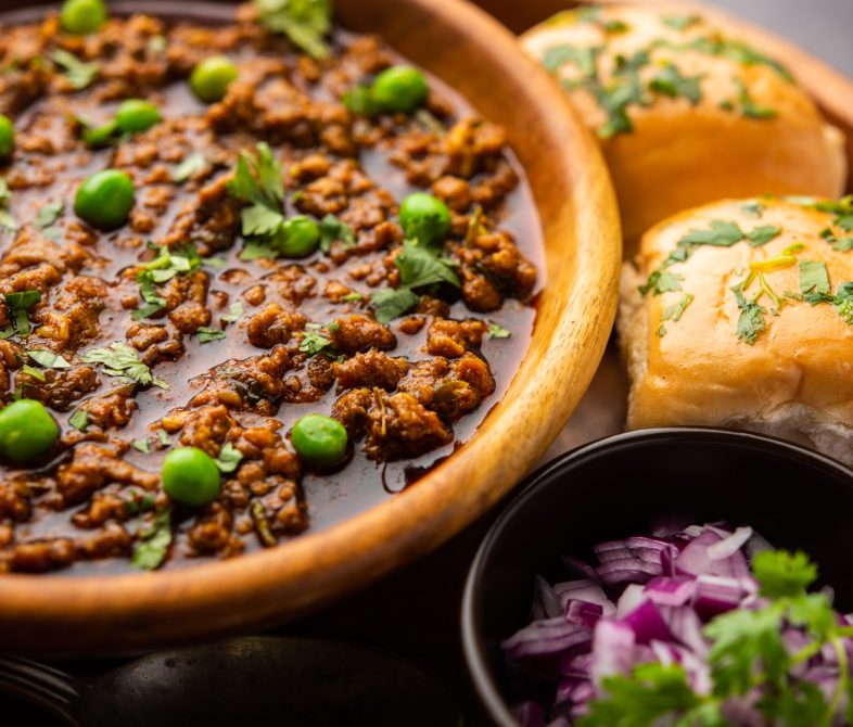 Mutton Kheema Pav OR Indian Spicy Minced Meat served with bread OR kulcha, garnished with green peas. Moody background. Selective focus